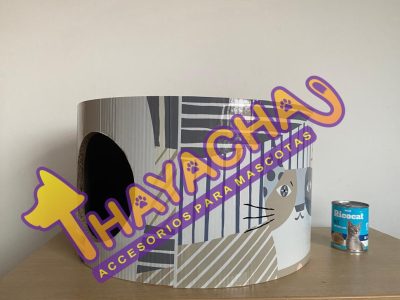 Cama cilíndrica para gatos con estampado de gatitos sobre mesa blanca