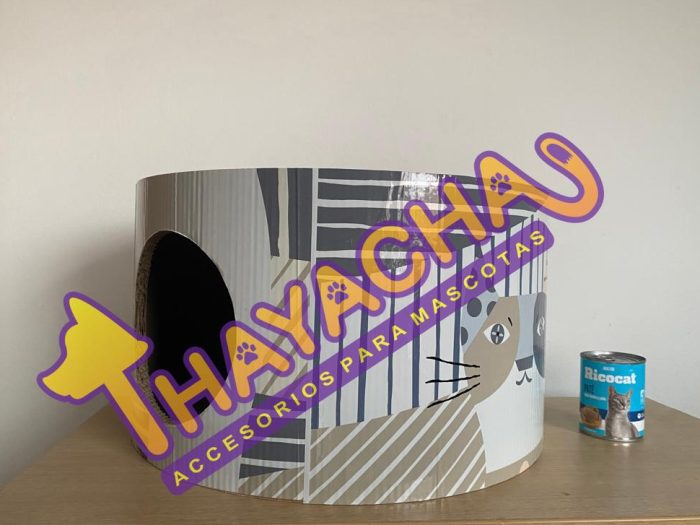 Cama cilíndrica para gatos con estampado de gatitos sobre mesa blanca